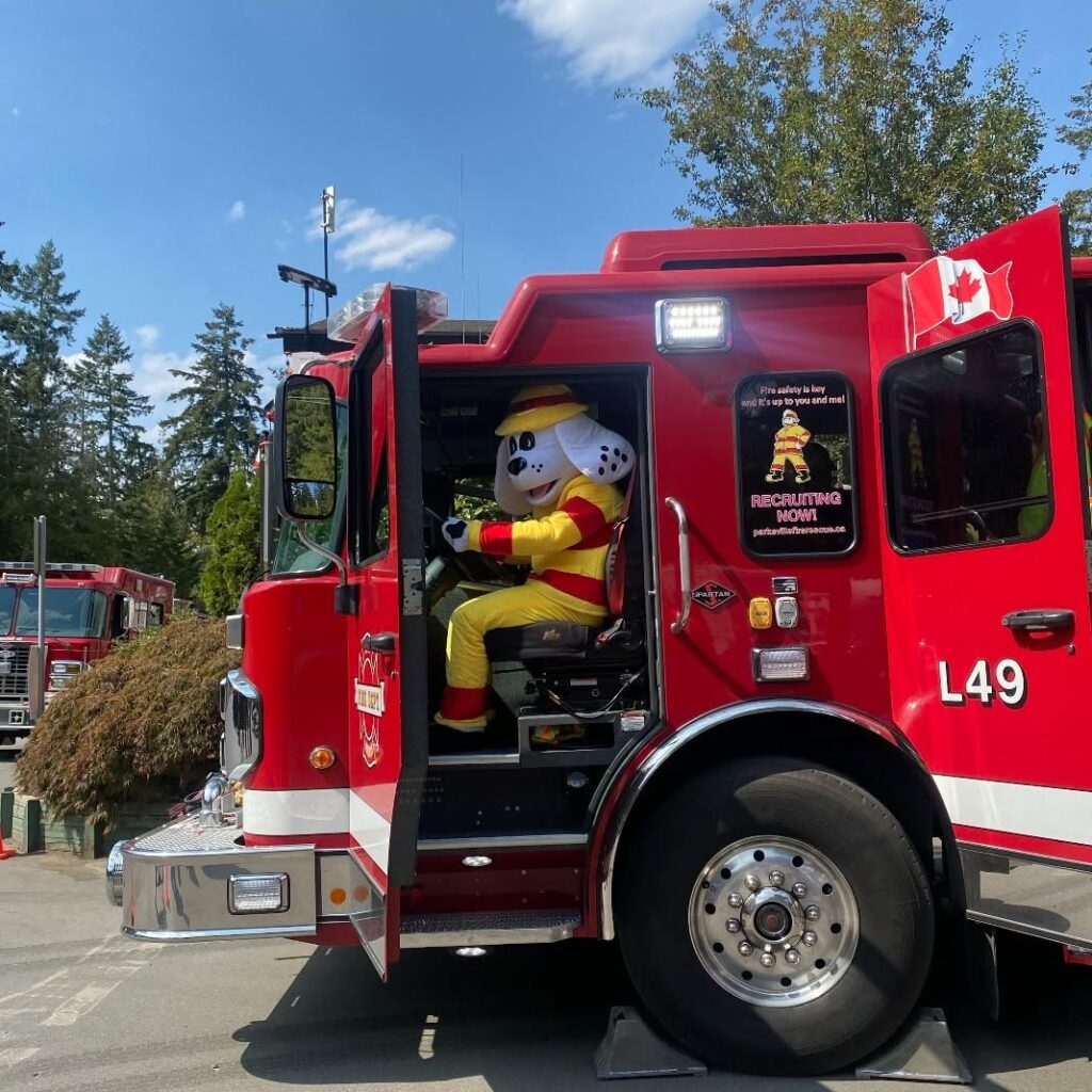 Sparky the Fire Dog mascot waving from the cab of Parksville Fire Rescue ladder truck L49